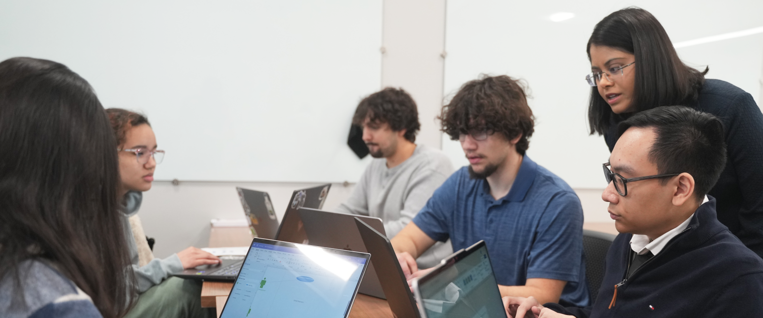 An instructor works with a group of students using laptops