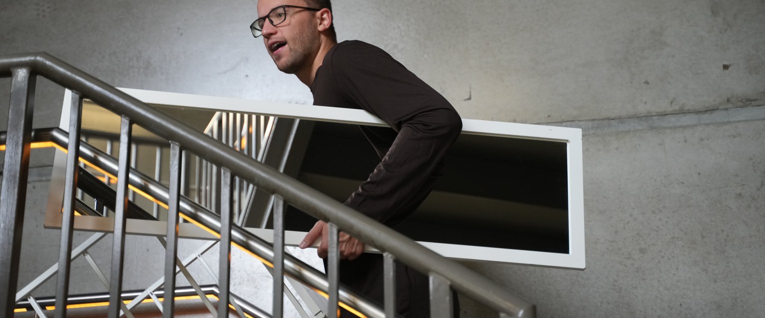 A student walking up a staircase holding a long mirror.