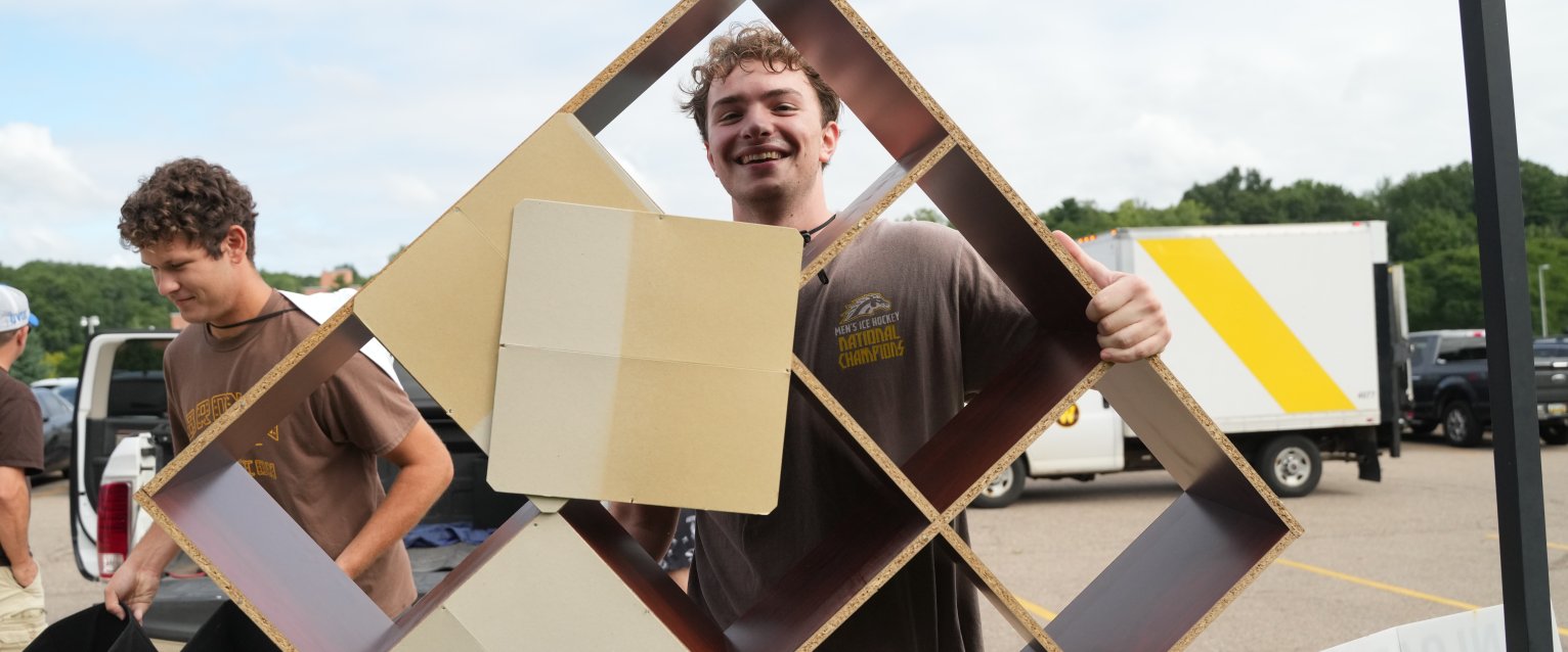 A student volunteer carrying a storage cube shelf.