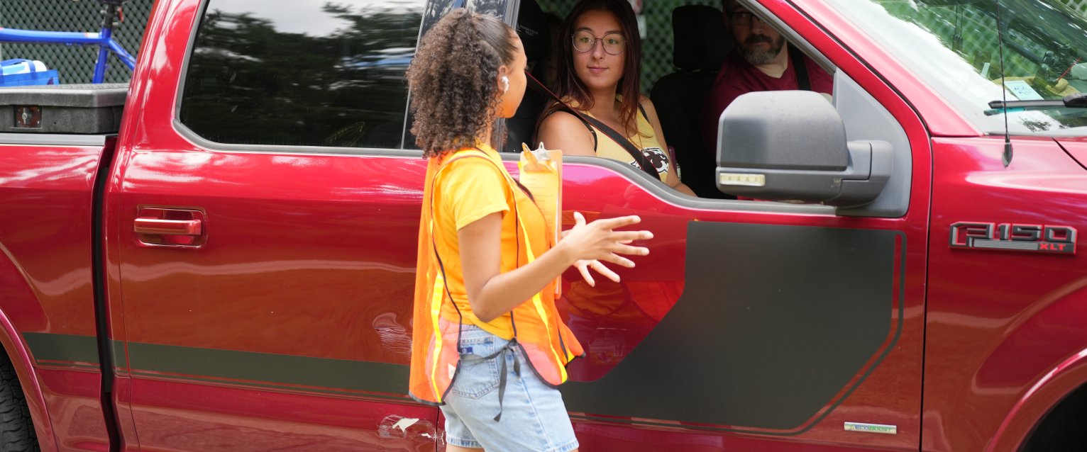 A student volunteer wearing an orange safety vest directs move-in traffic.