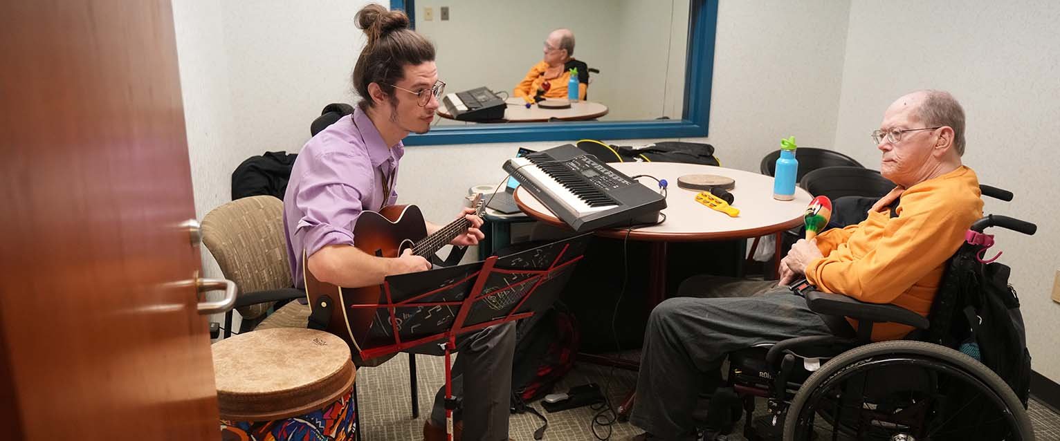 music therapy student holding a guitar and working with a client in a wheelchair