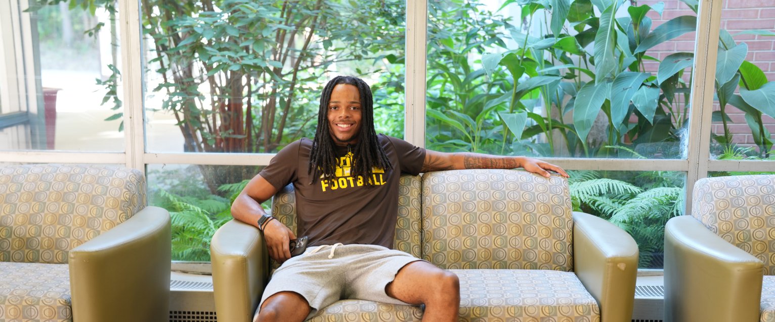 A student in a WMU football t-shirt sits on a couch in a residence hall lobby.