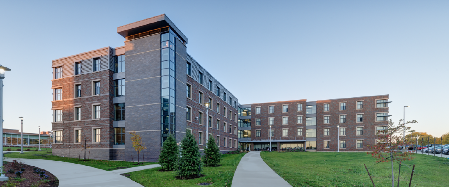 A multiple story brick residence hall at dusk. 