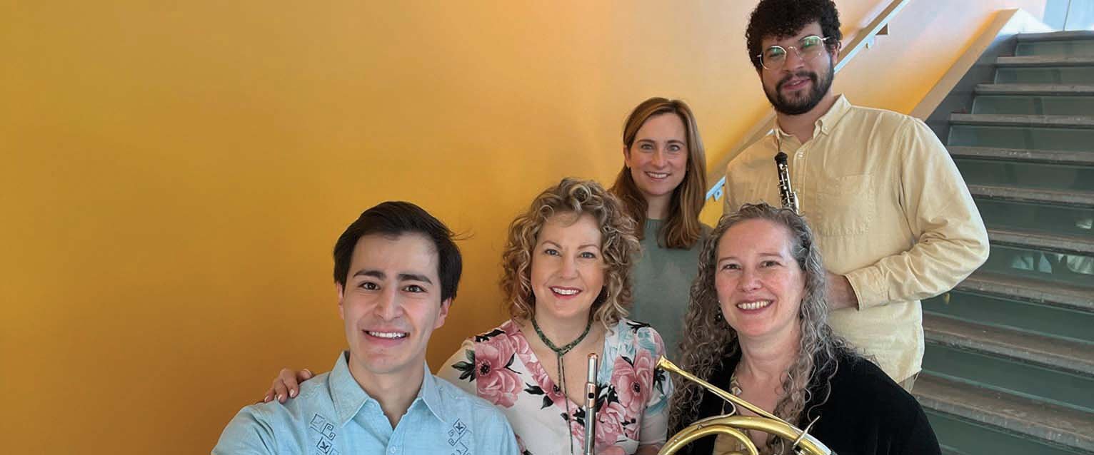 selfie photo of five musicians holding woodwind instruments and standing on a staircase