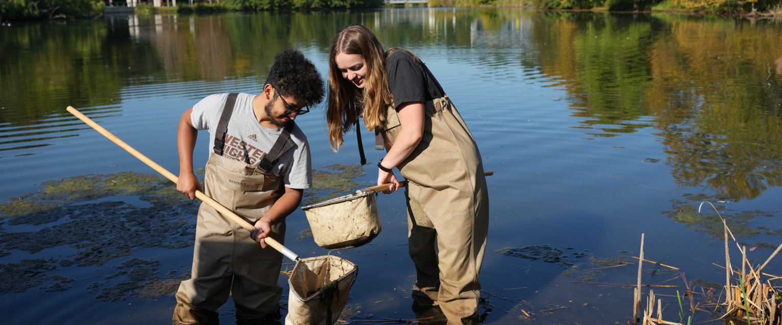 two students standing in a pond collecting a sample