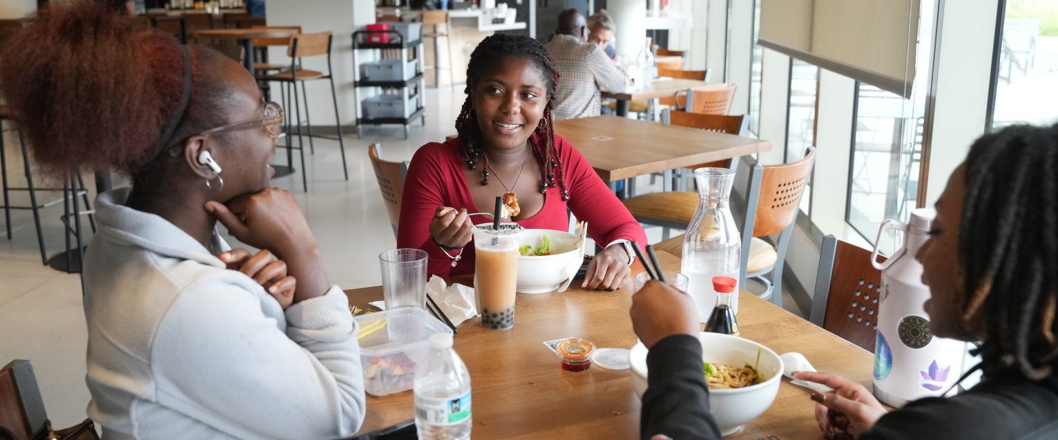 Three students sit at a table in a restaurant eating raman and drinking boba tea.