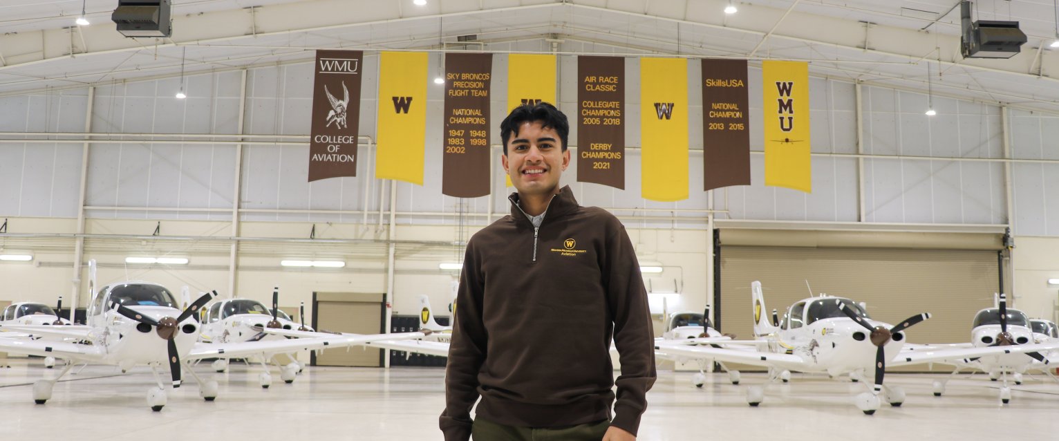 Student standing in plane hangar with planes.
