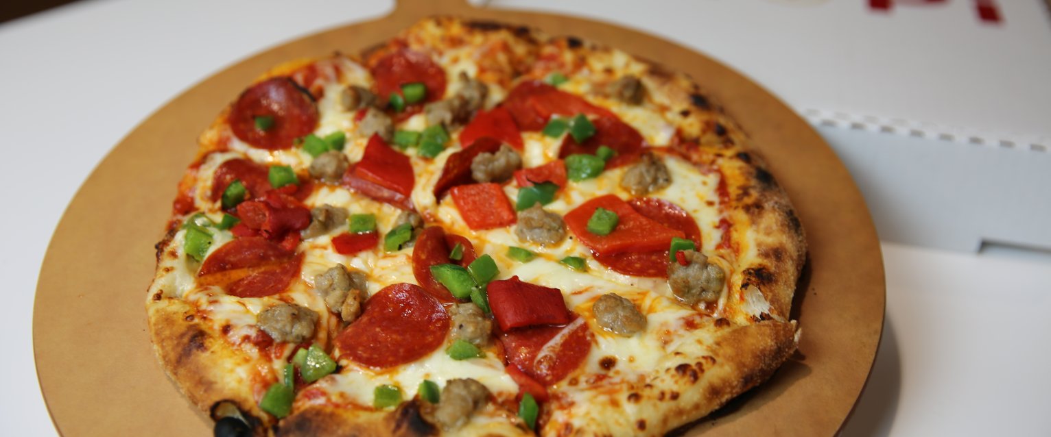 A pepperoni and sausage pizza with green peppers sits on a round serving tray beside a white MiPi carryout box.