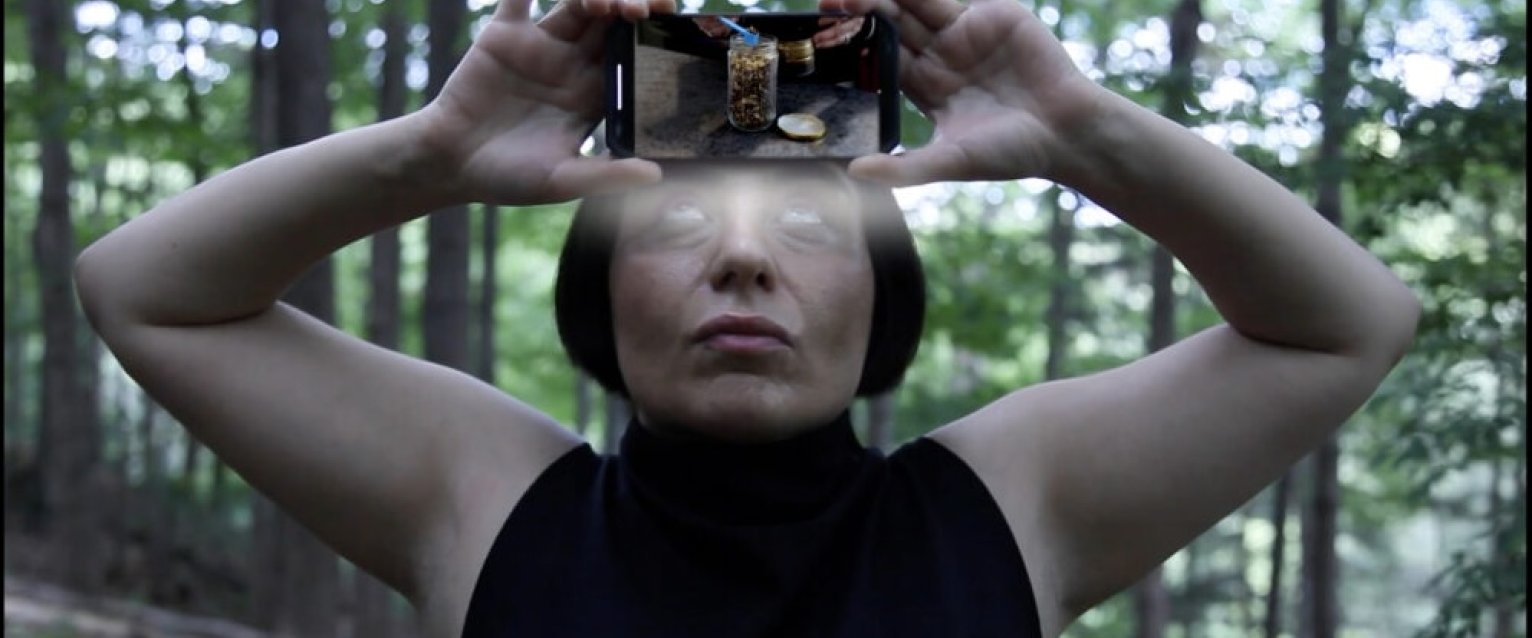 Rah Eleh holding phone to their forehead in the woods, a video is playing.