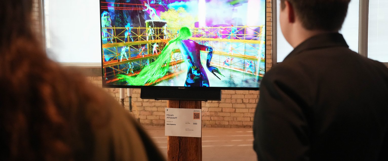 Gallery patrons looking at screen with Micah Alhadeff's work playing.