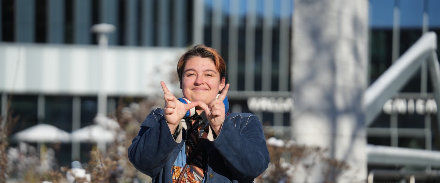 A student makes a W with their hands outside a snow covered Valley Dining Center.