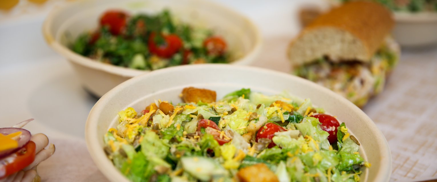 An assortment of salads, grain bowls, and sub sandwiches sitting on a white countertop.