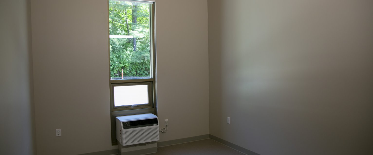 An interior shot of a Valley oaks residence hall room without furniture, featuring an air-conditioner in the window and a wood ceiling.