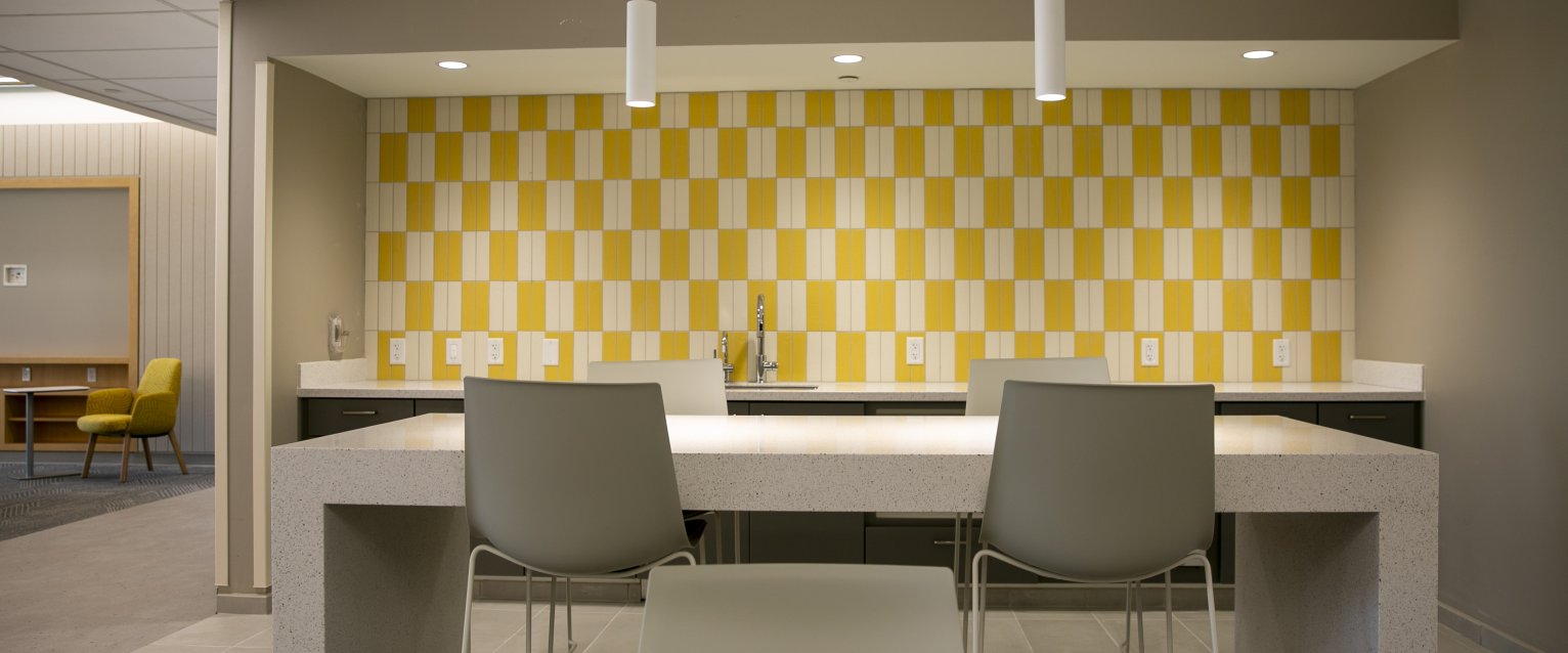 A Valley Oaks kitchenette with sleek white furniture against a yellow and white tiled wall.