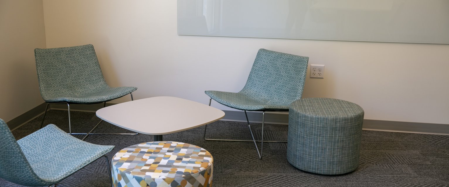 Three chairs and two short stools sit around a small white table in the corner of a Valley Oaks study lounge.