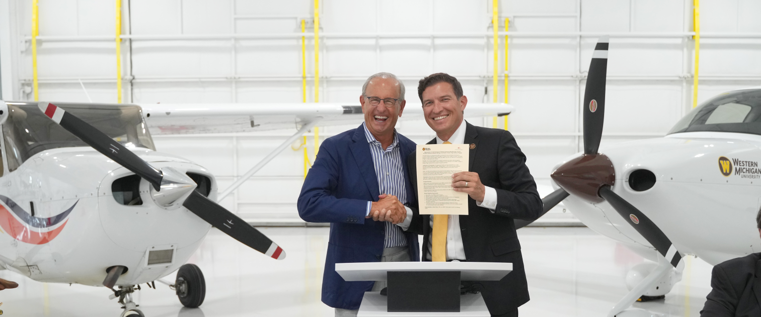 Dick DeVos and Russ Kavalhuna hold up an agreement inside an airplane hangar.