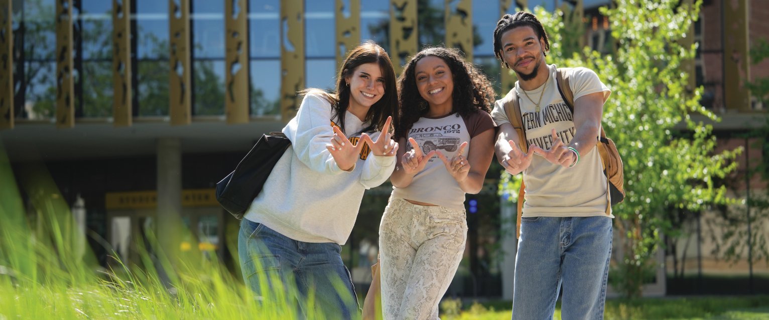 Three students pose in front of the Student Center wearing Western gear