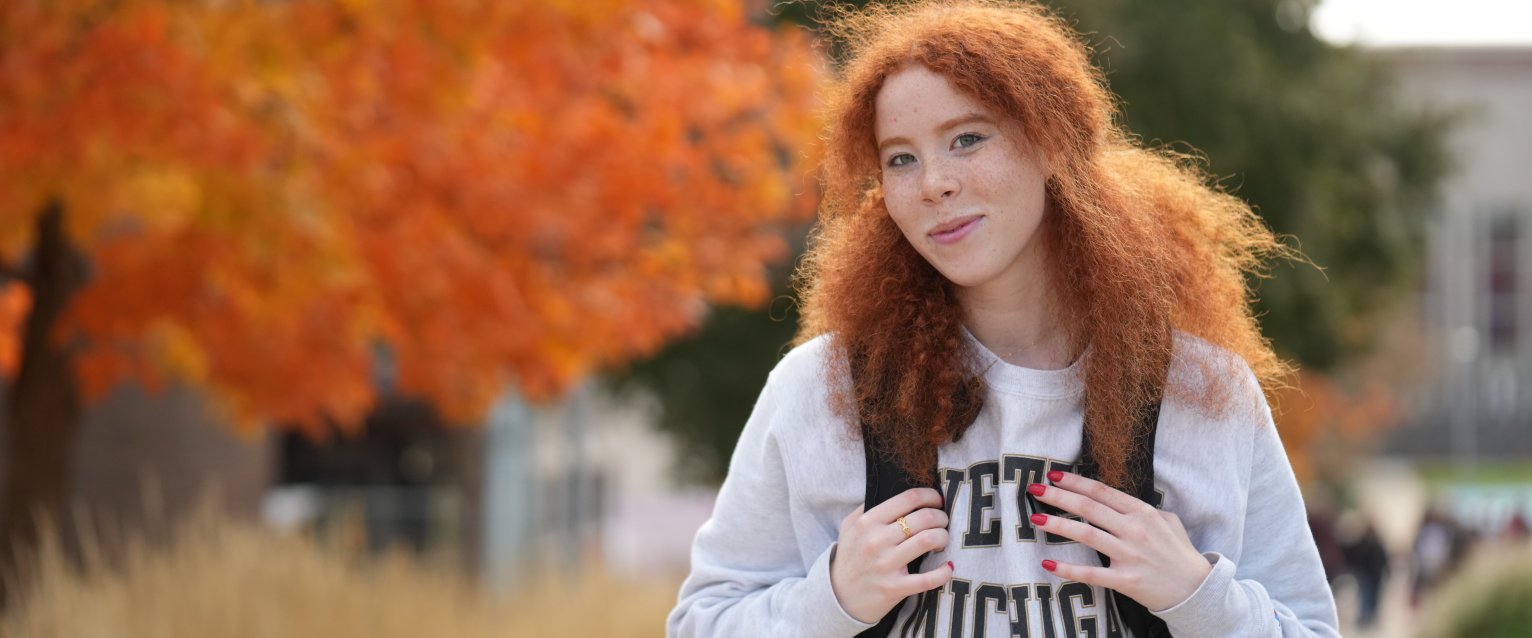 Student on Western campus smiles at camera, wearing a Western Michigan white sweatshirt.