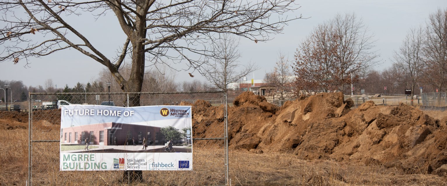 A sign that reads "Future Home of MGRRE Building" is attached to a portion of fence in front of the new MGREE Building site.