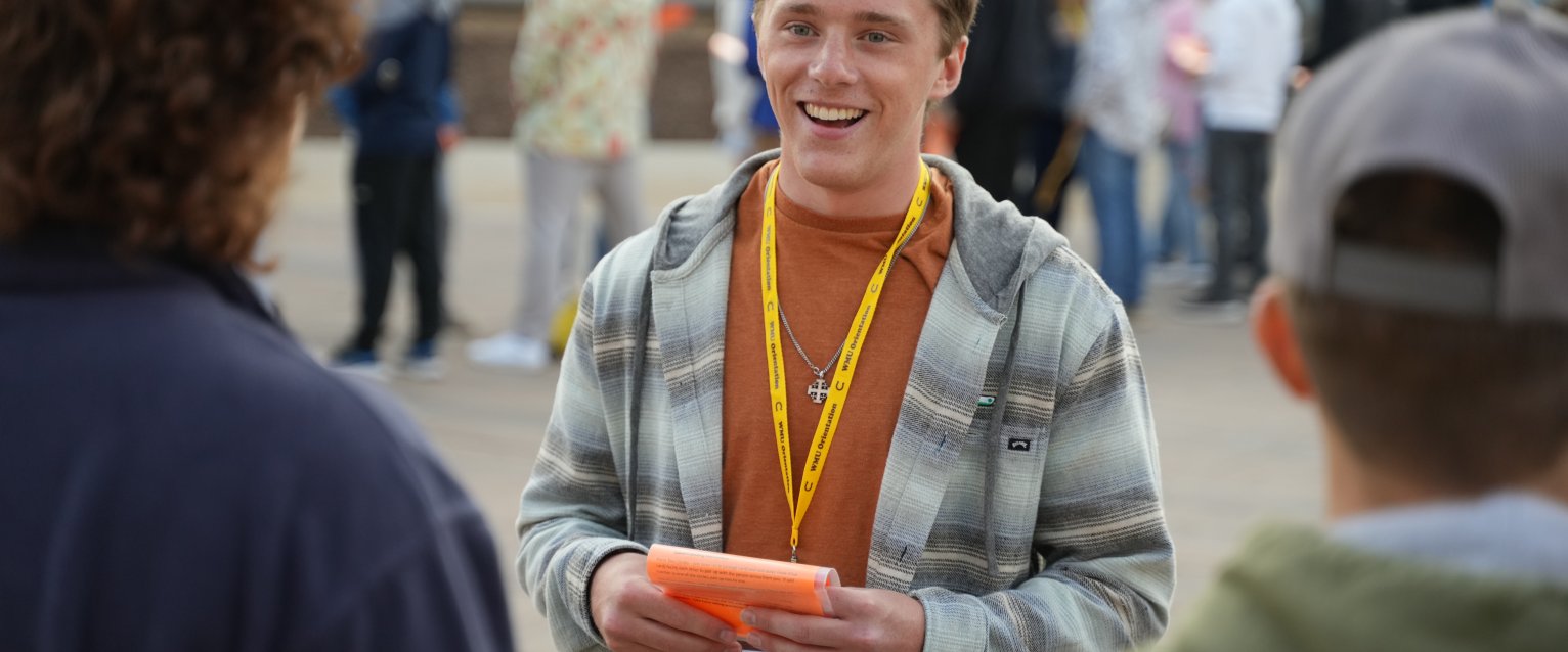 A smiling student wears a yellow WMU Orientation lanyard and talks to other students at an orientation activity.