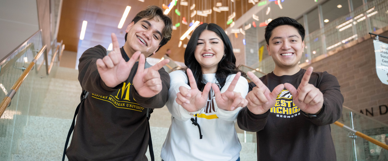Three students hold up Ws with their hands.