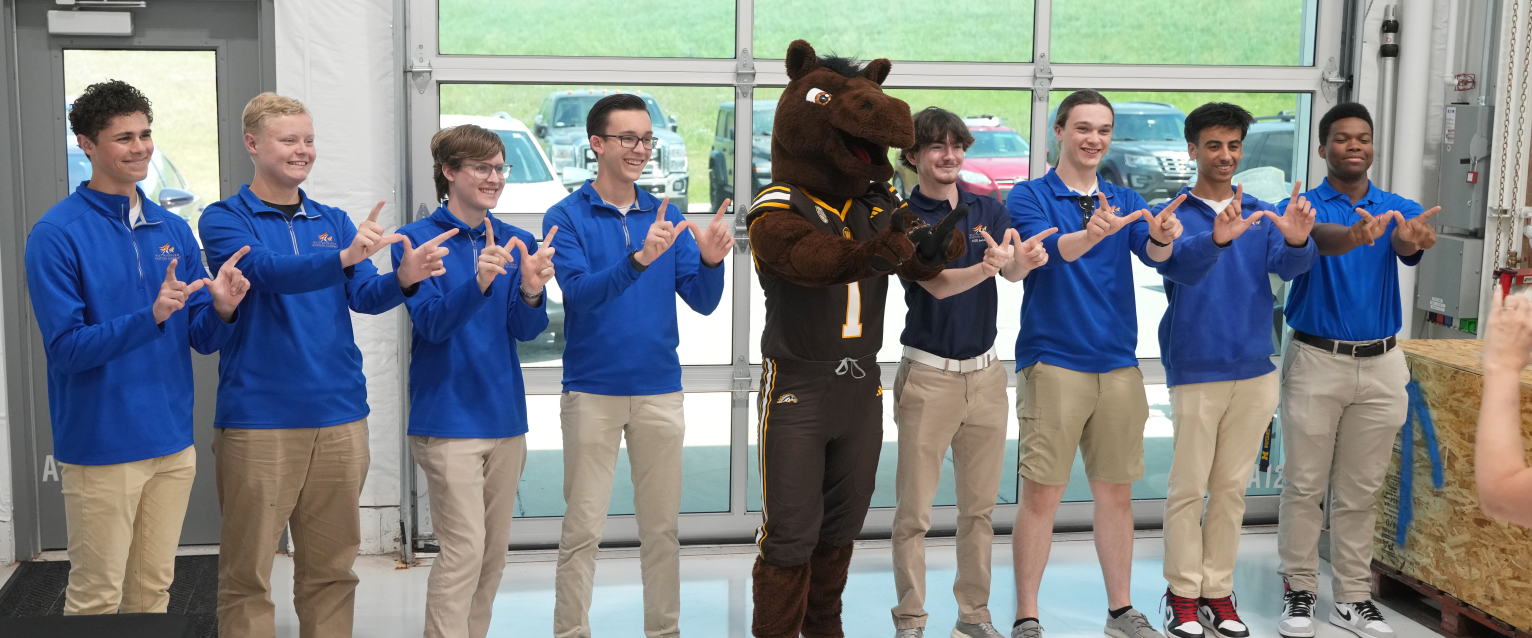 West Michigan Aviation Academy students throw up the "W" with their hands for a photo with Buster Bronco.