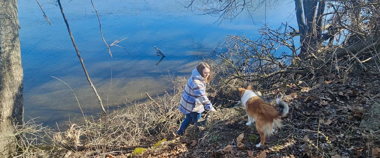 WMU student volunteer with a visiting Shelty dog during Kalamazoo river cleanup at Verberg Park.