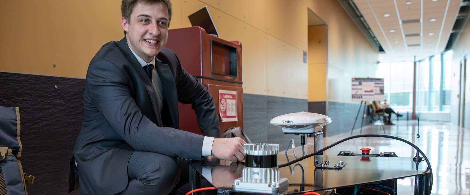 A student in a suit at the Senior Engineering Design Conference with a robot. 