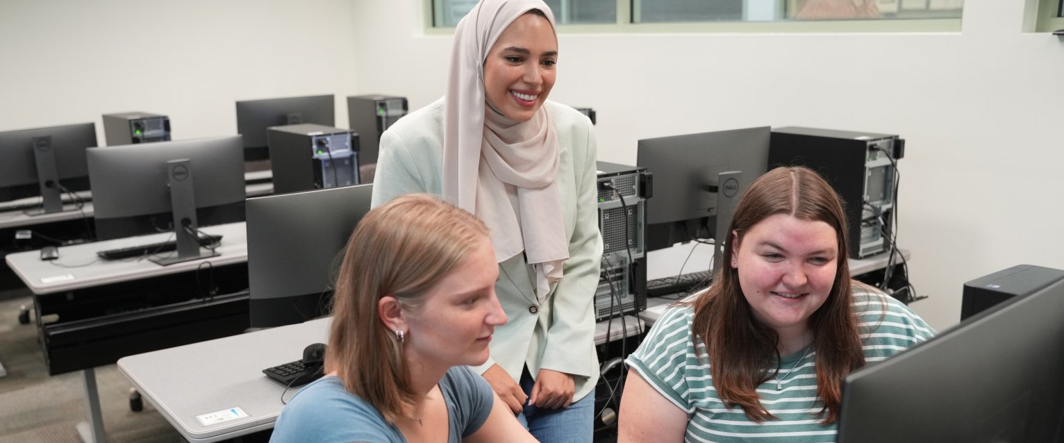 A professor helping students at a computer. 