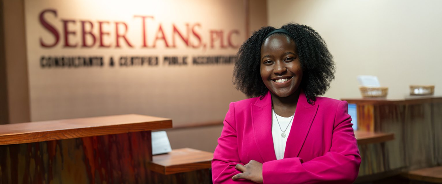 A student with arms crossed in front of the Seber Tans financial company sign