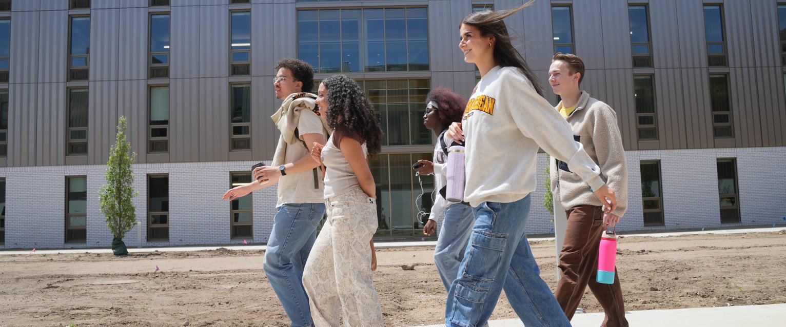 A group of Western students wearing WMU branded clothing walk on a sidewalk in the Valley Oaks courtyard. 