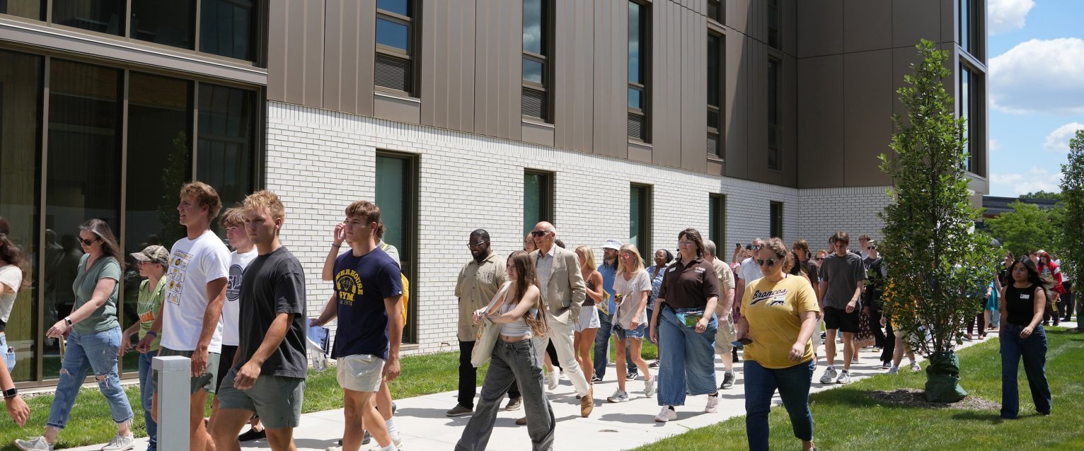 A crowd of ribbon-cutting attendees walks outside the new Valley Oaks residence hall.