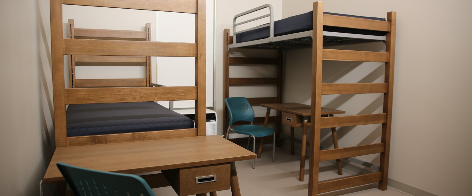 An undecorated Valley Oaks residence hall room with two lofted beds, two desks, and two teal desk chairs.