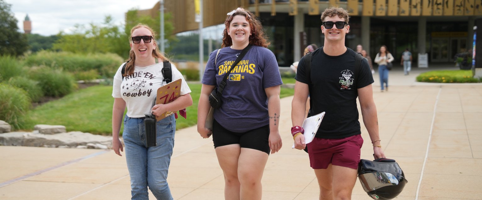 Three smiling students walking away from the Student Center. 