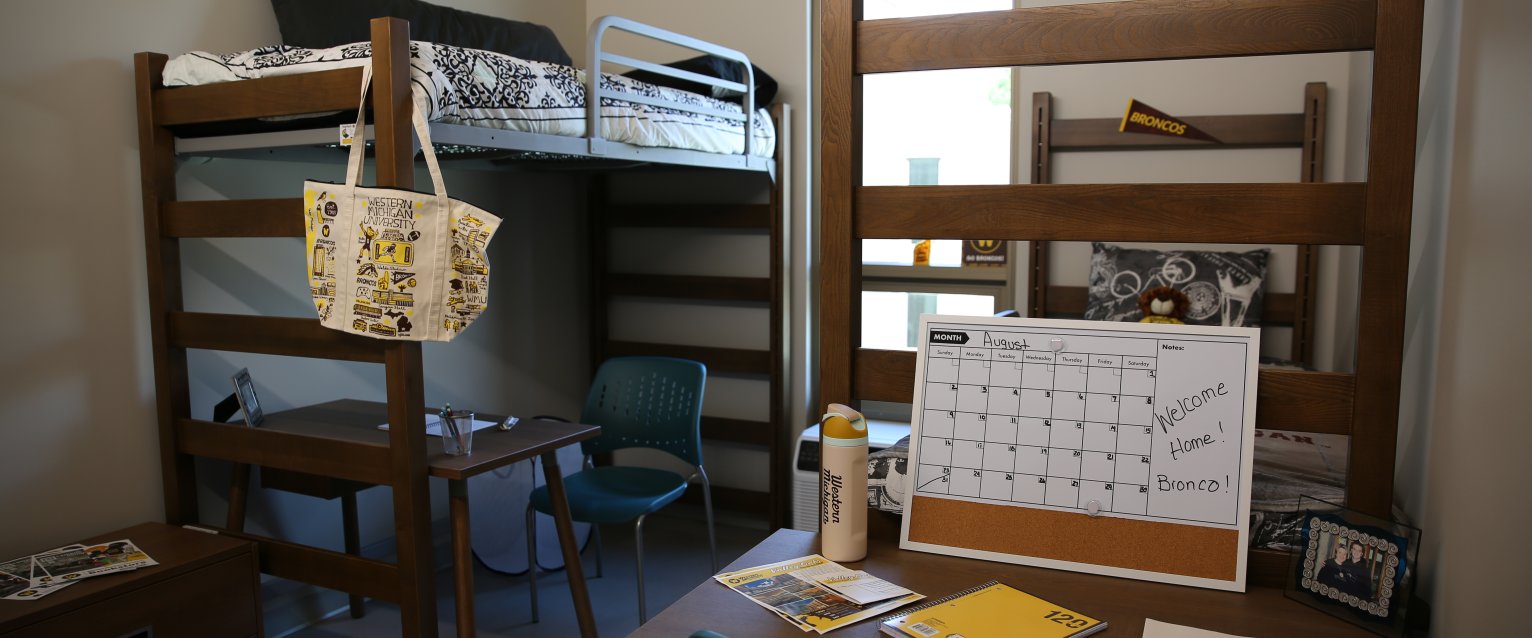 A decorated residence hall room with two lofted beds on either side of a tall window.