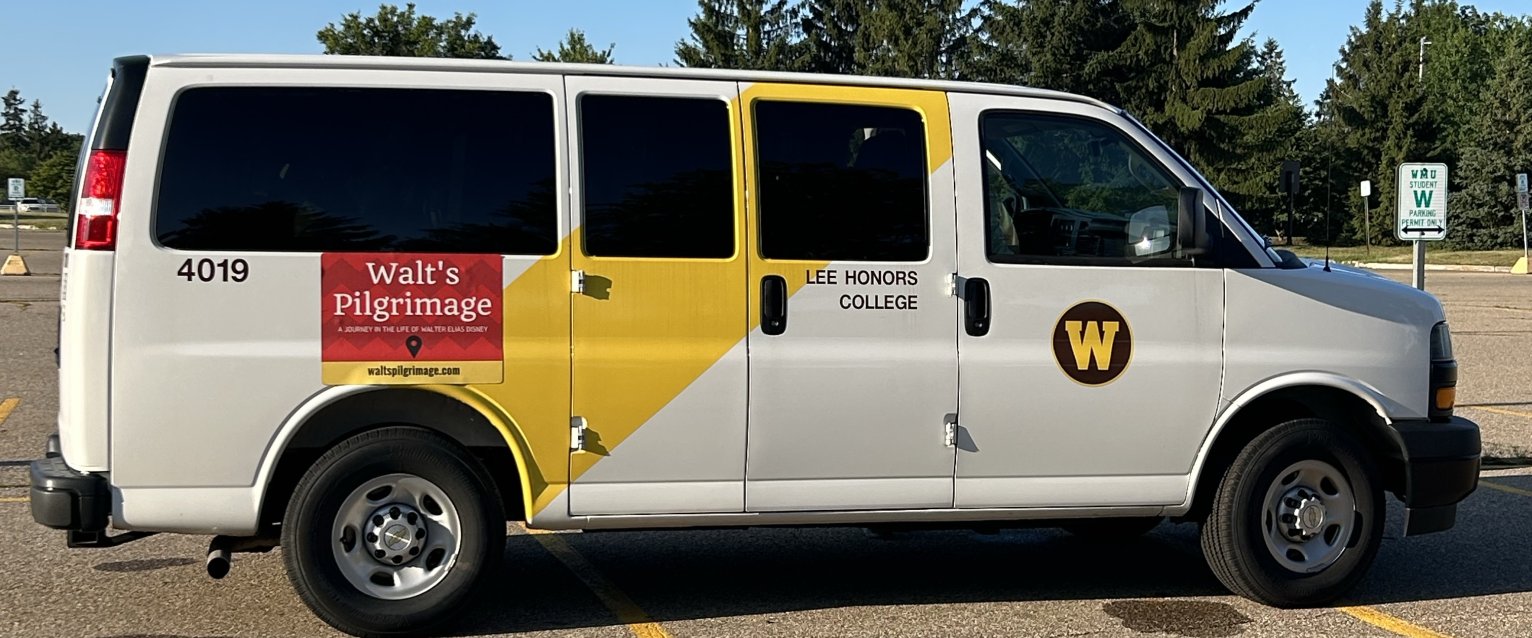 A Lee Honors College van sits in the parking lot, awaiting departure for the Study in the States course, Walt's Pilgrimage. There is a special Walt's Pilgrimage magnet on its side for the trip.