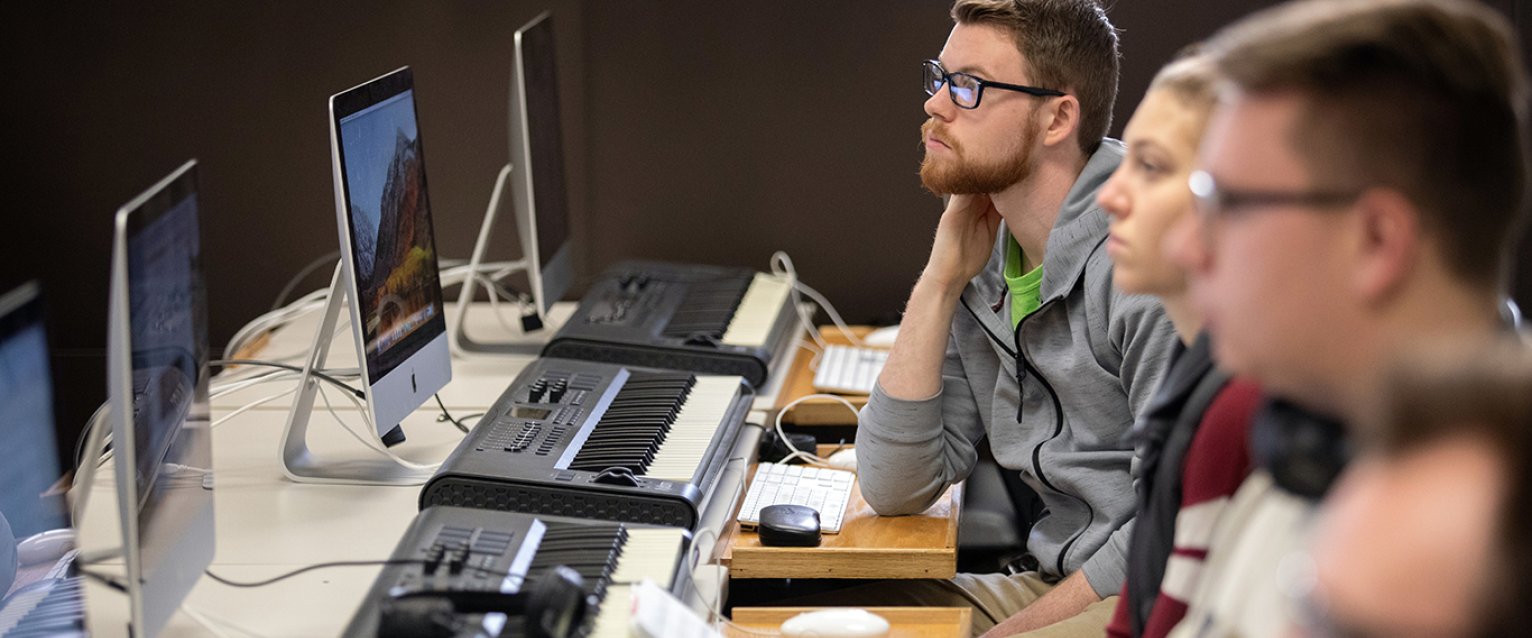 Music students paying attention at computers with keyboards in front of them.