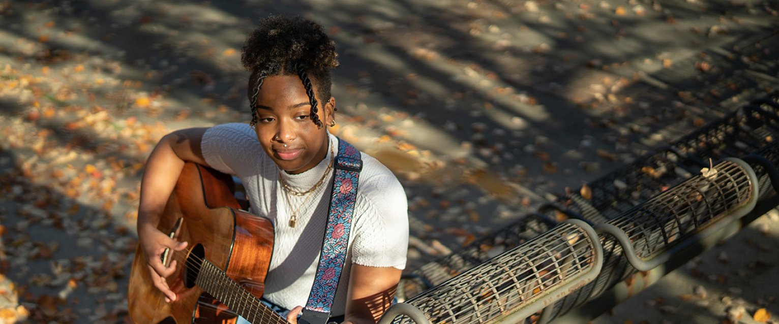 Music therapy student playing the guitar on a bench outside.