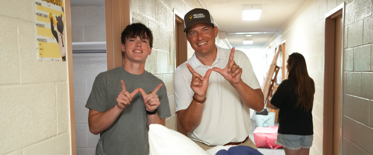 A student and President Russ Kavalhuna hold their hands in the shape of a W inside a residence hall.