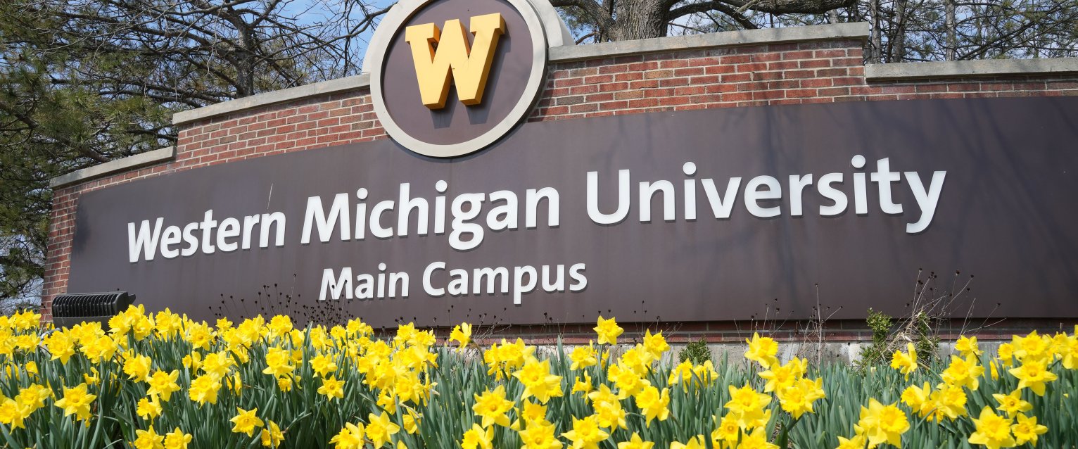 A photo of the WMU welcome area, a brick wall with the WMU logo and bright yellow daffodils in the front