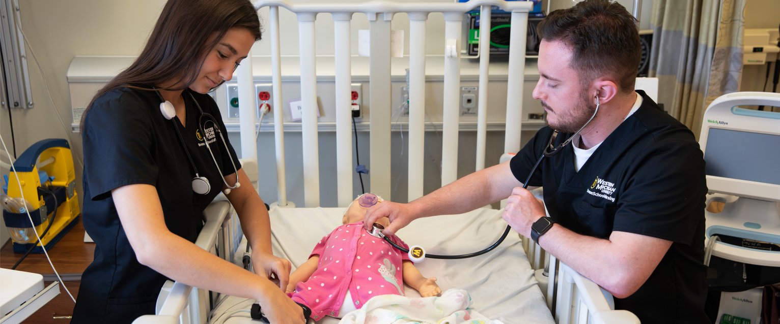 Two Bronson School of Nursing students checking on an infant dummy.