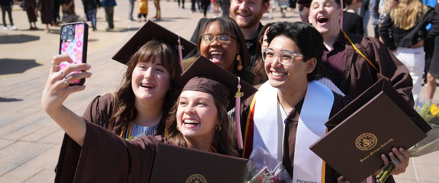 WMU grads in caps and gowns taking a photo on campus