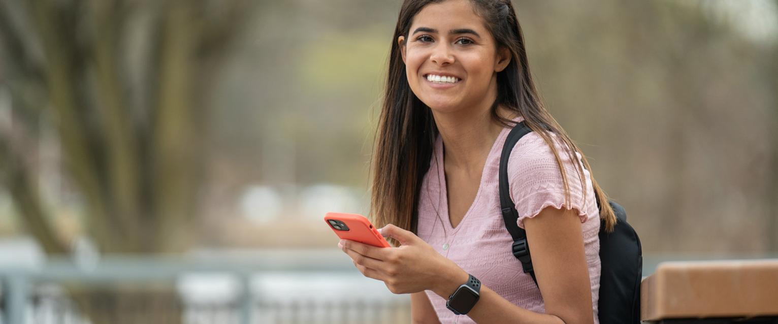 A student on their phone, pauses and smiles at the camera.