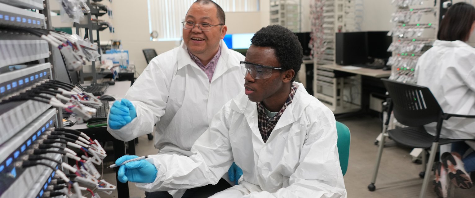 A professor and a student in a chemical lab, working on a project. They are both wearing white lab coats. 
