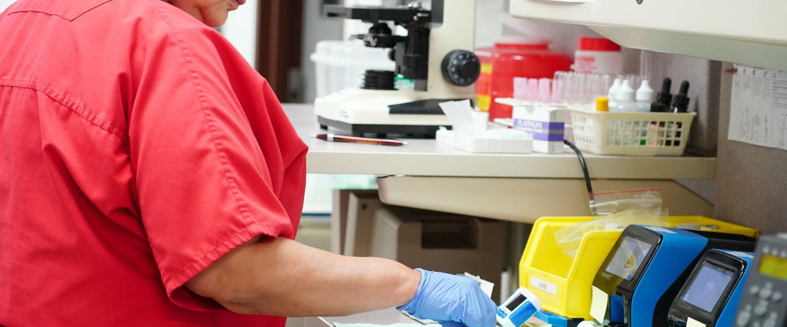 Medical Assistant manages testing of samples at table, with test machines
