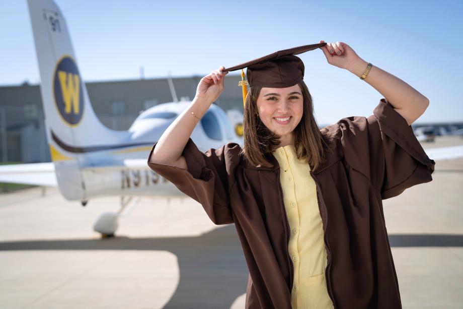 Grace Stachowiak poses in her graduation regalia in front of an airplane.