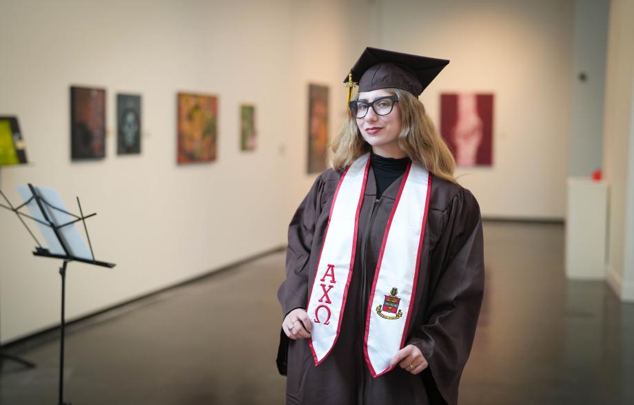 A portrait of Hope Donovan wearing graduation regalia in an art gallery.