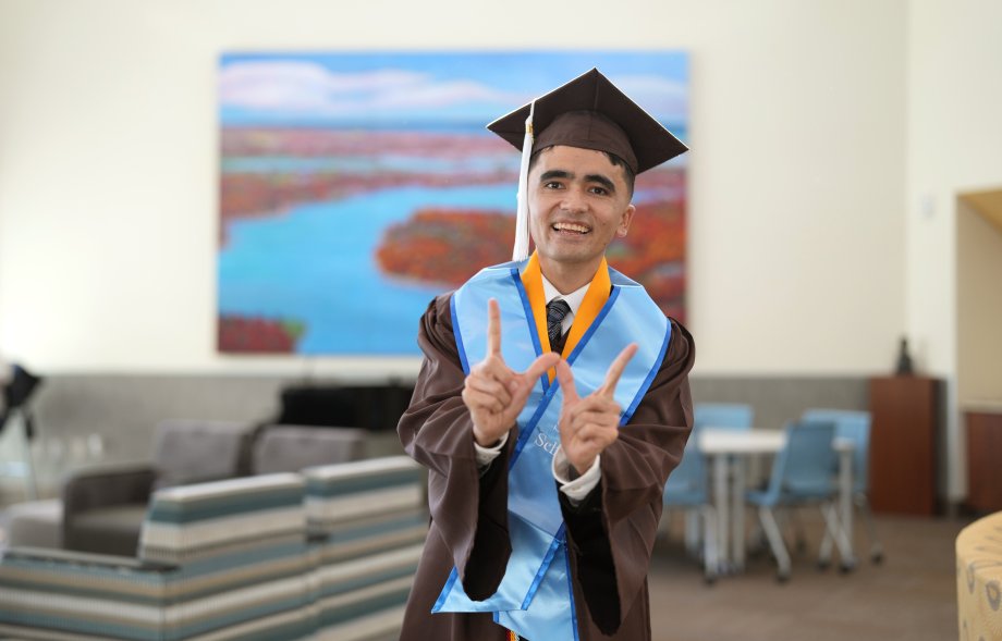 A portrait of Mehran Najafi in his graduation regalia holding up a W sign with his hands.