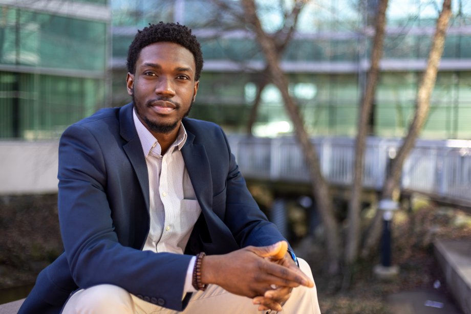 Yomi Nathan, a black man in a suit jacket, sitting outside of Floyd Hall on a bench.