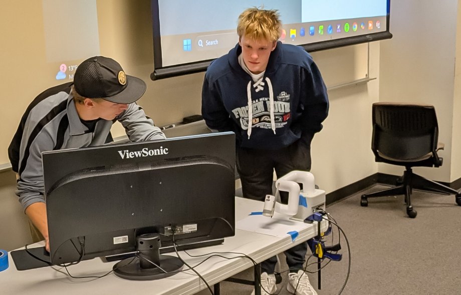 Torrey Cookman shows fellow student how to operate his Cobot